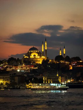 Günbatımından sonra, aydınlanan Süleyman Camii, Istanbuls silueti üzerinde yükseliyor. Altın Boynuz 'u geçen bir yolcu feribotu ve suda titreyen sıcak yansımalarla..