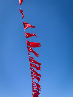 İstanbul 'da açık mavi gökyüzüne karşı rüzgarda dalgalanan Türk ulusal bayrakları, grafik çizgileri ve parlak renklerle yakın plan çekilmiş