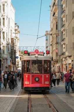 İstanbul, Türkiye - 6 Ekim 2025: Beyoğlu 'ndaki Istiklal Caddesi boyunca uzanan Kırmızı TaksimTunel tramvayı, mavi gökyüzüne karşı yaya caddesinde tarihi binalar ve müşteriler tarafından çerçevelendi..