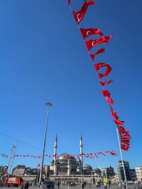 İstanbul, Türkiye - 6 Ekim 2025: Taksim Camii, Taksim Meydanı 'nda yürüyen insanlar, çerçevede asılı kırmızı Türk bayrakları ve açık mavi gökyüzüne karşı yükselen ikiz minareler