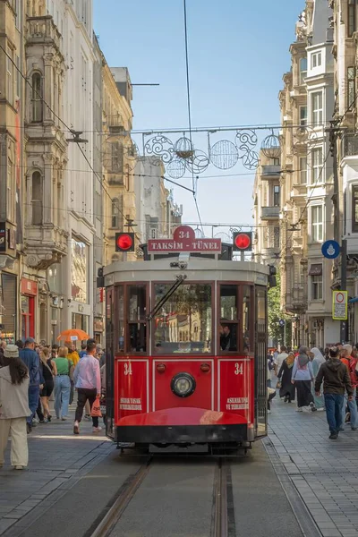 İstanbul, Türkiye - 6 Ekim 2025: Beyoğlu 'ndaki Istiklal Caddesi boyunca uzanan Kırmızı TaksimTunel tramvayı, mavi gökyüzüne karşı yaya caddesinde tarihi binalar ve müşteriler tarafından çerçevelendi..