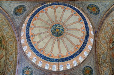 Türkiye 'nin İstanbul kentindeki Mavi Cami' nin süslü ana kubbesine bakıyorum. Çiçek desenleri, Arap kaligrafisi ve yumuşak ışıkla parlayan boyalı camlardan oluşan bir halka.