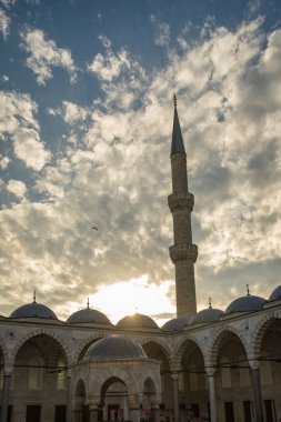 İstanbul, Türkiye 'deki Sultanahmet Camii' nin (Mavi Cami) avlusunda, bulutlarla dolu dramatik bir akşam gökyüzü altında minare silueti, kubbeleri ve kemerlerle ışıklandırılmış manzara