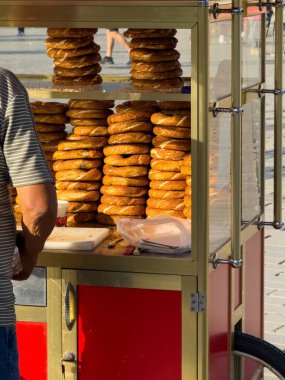 İstanbul, Türkiye 'de öğleden sonra ışığında çalışan bir satıcı olarak cam bir sokak arabasında üst üste yığılmış altın, susamlı simit