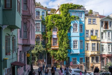 İstanbul, Türkiye - 8 Ekim 2025: Balat 'ta renkli tarihi evleri ve sarmaşık kaplamalı cephesi olan kaldırım taşlı bir sokakta kalabalık