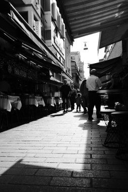 İstanbul, Türkiye - 8 Ekim 2025: İnsanlar Kadıköy 'de siyah-beyaz restoranlar ve tentelerle dolu dar bir yaya caddesi boyunca yürüyor