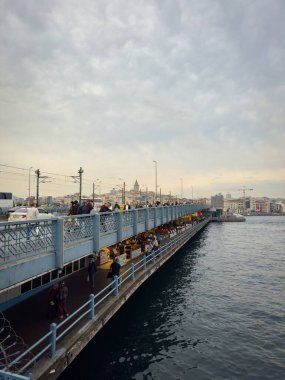 İstanbul, Türkiye - 7 Ekim 2026: Galata Köprüsü boyunca yukarıdaki yaya ve aşağıdaki sahil restoranları, ufuk çizgisi ve suyun üzerindeki uzaklıktaki Galata Kulesi 'ne bakın