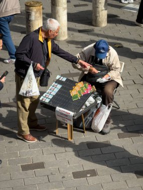 İstanbul, Türkiye - 8 Ekim 2025: Sokak satıcısı Kadıköy, İstanbul, Türkiye 'de kalabalık bir meydanda yoldan geçenlere piyango bileti sattı