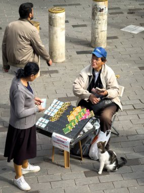 İstanbul, Türkiye - 8 Ekim 2025: Sokak satıcısı Kadıköy, İstanbul, Türkiye 'de kalabalık bir meydanda yoldan geçenlere piyango bileti sattı