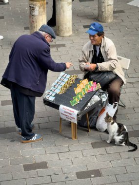 İstanbul, Türkiye - 8 Ekim 2025: Sokak satıcısı Kadıköy, İstanbul, Türkiye 'de kalabalık bir meydanda yoldan geçenlere piyango bileti sattı