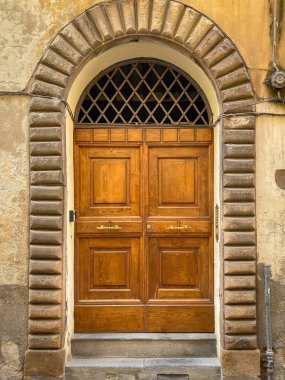 İtalya 'da eski bir binaya taş bir kemer ve yıpranmış bir sıva tarafından çerçevelenmiş klasik ahşap bir çift kapı.