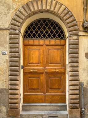 İtalya 'da eski bir binaya taş bir kemer ve yıpranmış bir sıva tarafından çerçevelenmiş klasik ahşap bir çift kapı.