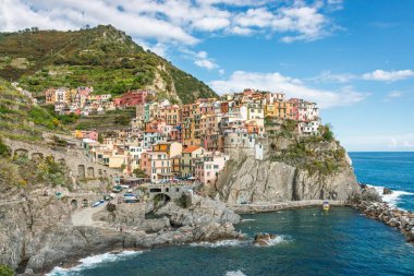 Manarola 'nın Cinque Terre boyunca manzarası Liguria, İtalya' da Akdeniz 'in yukarısındaki kayalık bir sahil şeridinde renkli evler bulutlu mavi gökyüzüne karşı.