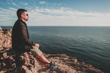 Orta yaşlı bir adam uçurumun kenarında, deniz manzaralı.