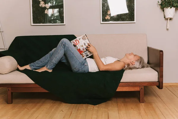 Junge Blonde Frau Liest Die Zeitschrift Auf Dem Sofa — Stockfoto