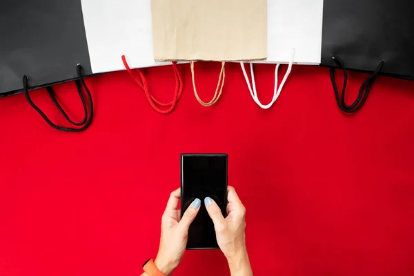 黑色星期五甩卖 女人在智能手机上用红色背景购物袋进行网上购物 — 图库照片