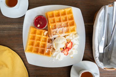 Üzerine çilek şurubu, dondurma, çırpılmış krema ve badem dilimi konmuş waffle.