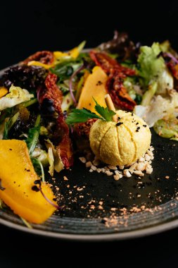 Balkabaklı sonbahar salatası ve siyah arka planda güneşte kurutulmuş domates.