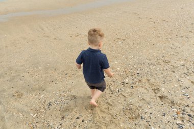 Küçük çocuk sahile yakın kumsalda oynuyor.