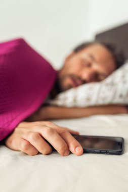 Cep telefonunu tutarken uyuyan genç ve yakışıklı bir adam. Telefonun ekranı kapalı.