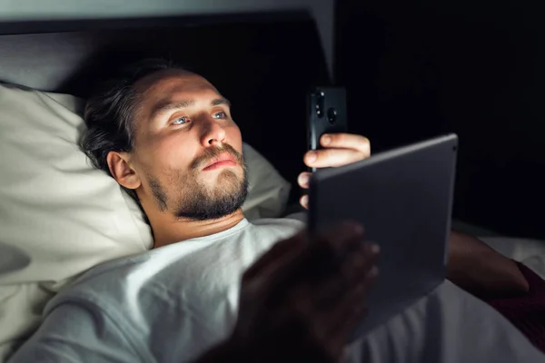 Genç Sakallı Adam Yatağında Uzanmış Telefonuna Tabletine Bakıyordu — Stok fotoğraf