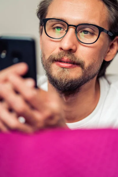 Guapo Joven Sonriente Con Gafas Acostado Cama Mientras Sostiene Teléfono —  Fotos de Stock