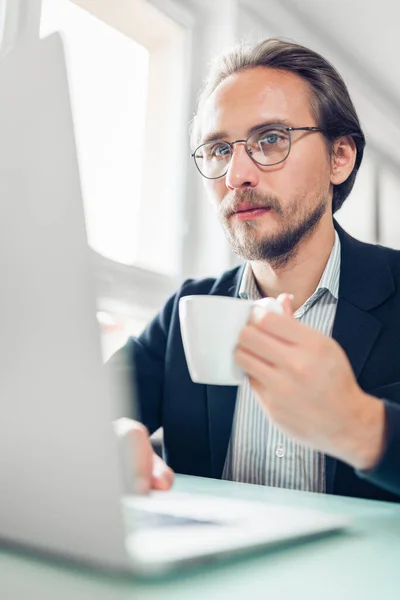 Foto Joven Guapo Enfocado Sentado Junto Escritorio Trabajando Computadora Mientras —  Fotos de Stock