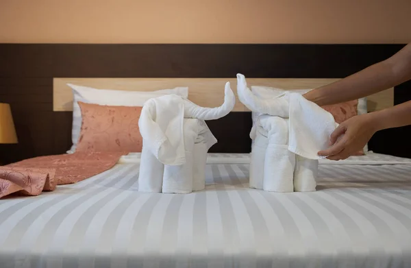 ホテルのメイドクリーニングベッドルームサービス シーツの上に象のような白いバスタオルを折り畳む手のクローズアップ — ストック写真