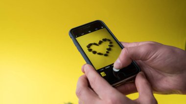 Sarı arka planda kalbi olan akıllı bir telefonu tutan el.