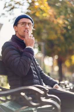 Genç bir adam güzel bir sonbahar gününde bankta sigara içiyor..