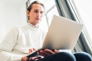 Genç adam taşınabilir bilgisayarına bakıyor..