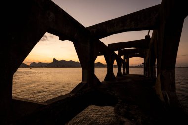 Rio de Janeiro, Brezilya 'daki kalenin beton yapısına çerçevelenmiş Corcovado Dağı' na güzel bir okyanus gün batımı manzarası