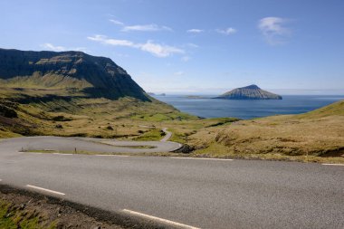 Asfalt kıvrımlı yol manzarası yeşil kayalık tepelerle çevrili ve denize açılıyor.