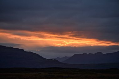 Parlak günbatımı gökyüzünün altında kayalık dağ sıraları olan Highland Vadisinin görkemli manzarası.