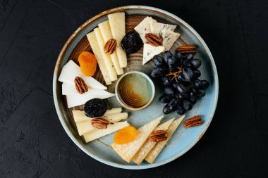 Siyah arka planda çeşitli peynirler bulunan peynir tabağı.