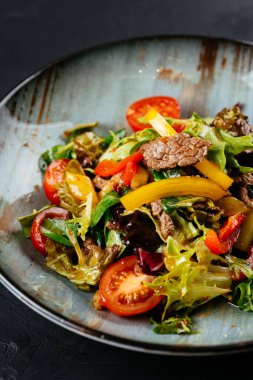 Siyah arka planda mermer biftekli sıcak salata.