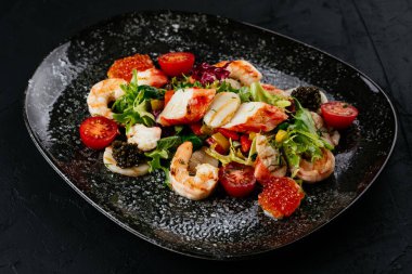 Siyah arka planda karides, sebze ve yengeç etli salata.