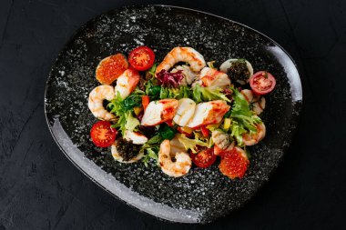 Siyah arka planda karides, sebze ve yengeç etli salata.