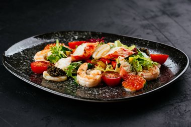 Siyah arka planda karides, sebze ve yengeç etli salata.