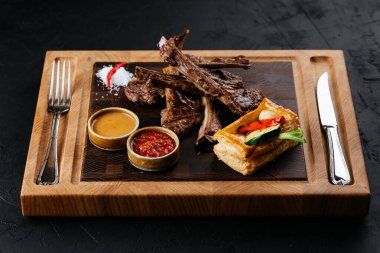 Izgara kuzu pirzola, sebzeli ve soslu siyah arka plan.