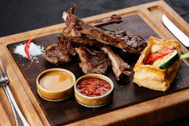 Izgara kuzu pirzola, sebzeli ve soslu siyah arka plan.