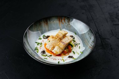 Siyah arka planda sebzeli ve soslu ızgara morina filetosu.