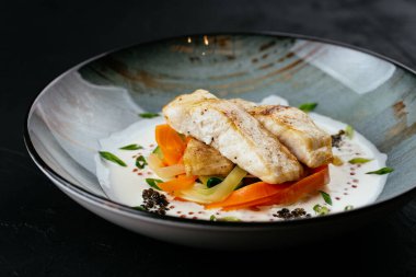 Siyah arka planda sebzeli ve soslu ızgara morina filetosu.