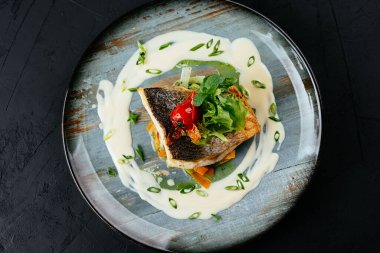 Siyah arka planda sebzeli ve soslu ızgara morina filetosu.