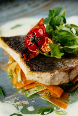 Siyah arka planda sebzeli ve soslu ızgara morina filetosu.