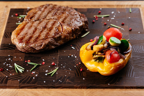 marbled beef steak with vegetables and sauce on a black background