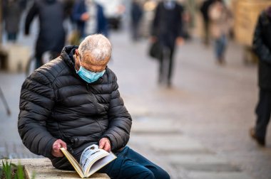 Terni, İtalya 19 Kasım 2020: Tıp maskeli adam açık havada kitap okuyor.
