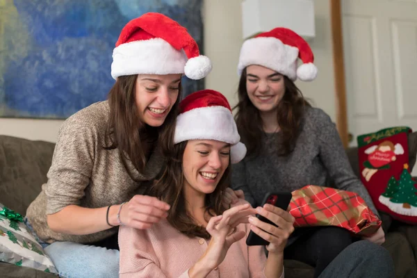 Three college-aged sisters in Santa hats looking at cell phone