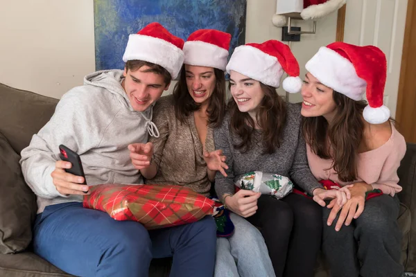 Four college-aged siblings wearing Santa hats look at selfies on