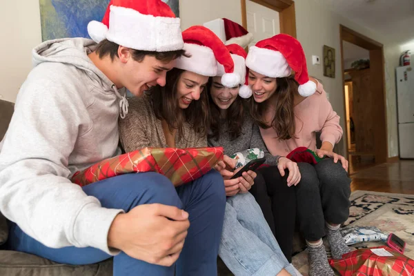 Four college-aged siblings wearing Santa hats look at selfies on